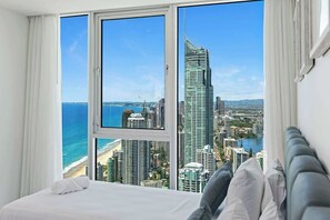 A hotel room with a large window offering a cityscape view, a bed, and a view of the ocean. - Hiltons Ocean Crown 49 (Surfers Paradise)