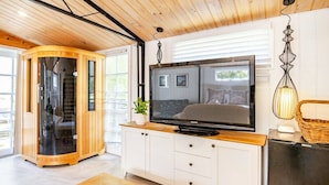 Ein modernes Wohnzimmer mit großem Flachbildfernseher, Holzschränken, einer Glas-Sauna und einem Essbereich mit Tisch und Stühlen.