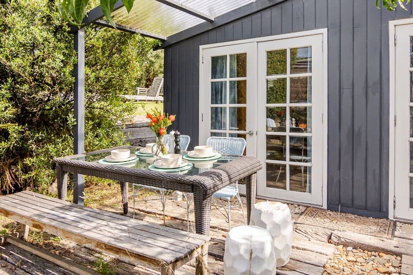 Un coin repas avec une table dressée pour quatre personnes, une chaise en osier et un banc.