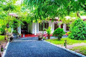 A building with a red roof, surrounded by lush greenery and potted plants. - Thathsara Holiday Inn (Sigiriya,)