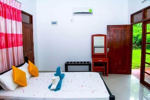A hotel room with a bed, a mirror, a small table, and an air conditioning unit on the wall. - Thathsara Holiday Inn (Sigiriya,)
