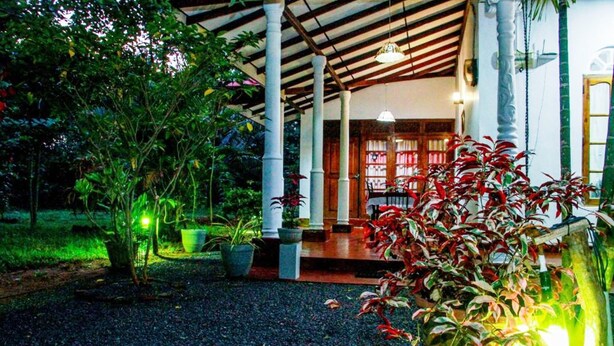A covered outdoor area with a gravel path, potted plants, and a wooden structure with a roof. - Thathsara Holiday Inn (Sigiriya,)