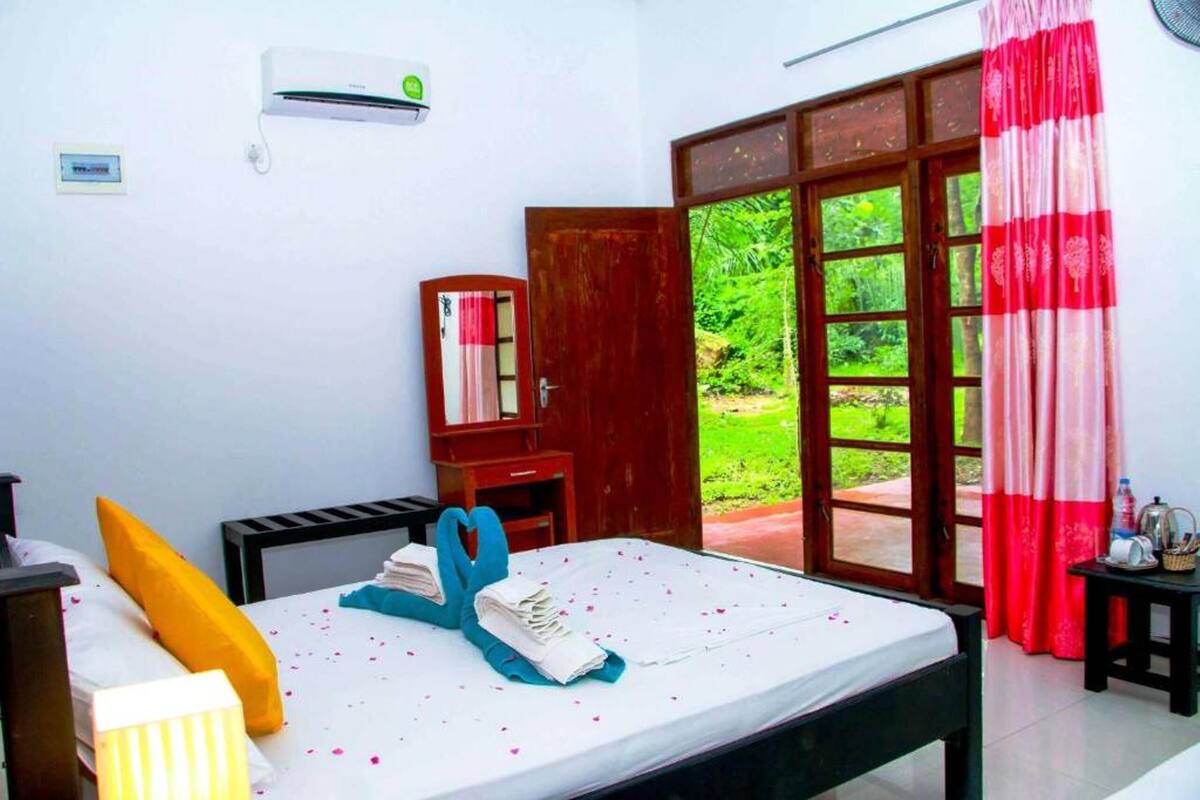 Quarto com cama, escrivaninha, guarda-roupa e janela com vista para o verde.