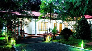 A building with a red-tiled roof, surrounded by lush greenery and illuminated by green lights. - Thathsara Holiday Inn (Sigiriya,)