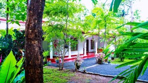 A building with a red roof and white walls, surrounded by lush greenery and potted plants. - Thathsara Holiday Inn (Sigiriya,)