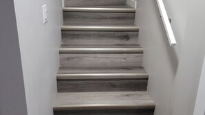 Un escalier avec des marches en bois et des rampes blanches, menant à un palier.