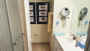 Een badkamer met een douche, twee wastafels, een spiegel en wanddecoraties van ingelijste visillustraties.