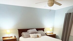 Een slaapkamer met een bed, twee nachtkastjes, een plafondventilator en een raam met gordijnen.