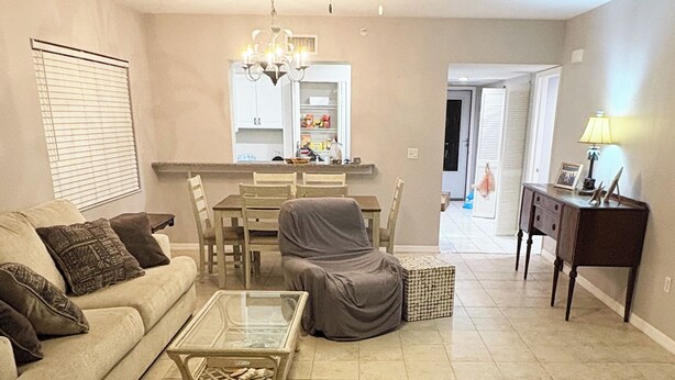Een woonkamer met een bank, een glazen salontafel en een stoel. Er is een eethoek met een tafel en stoelen. Een plafondventilator is zichtbaar, en een lamp staat op een bijzettafeltje.