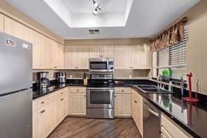 Una cucina moderna con mobili chiari in legno, elettrodomestici in acciaio inossidabile e un piano di lavoro nero.