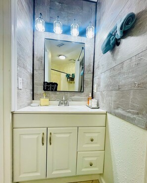 A bathroom with a white vanity, a mirror, and three hanging lights. - Sun & Sand condo retreat (Panama City Beach)