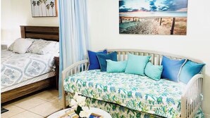 A bedroom with a bed, a sofa, a ceiling fan, a wall-mounted picture, and a small table with a vase and book. - Sun & Sand condo retreat (Panama City Beach)