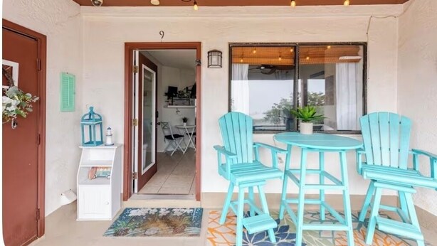 A covered outdoor seating area with turquoise chairs and a small table, a door leading to an interior space, and a window with a view. - Sun & Sand condo retreat (Panama City Beach)
