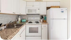 A kitchen with white cabinets, a microwave, a stove, a refrigerator, and a sink. - Sun & Sand condo retreat (Panama City Beach)