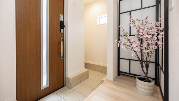 A hallway with a wooden door, a potted plant with pink flowers, and a sliding door with a black frame.