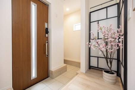 A hallway with a wooden door, a potted plant with pink flowers, and a sliding door with a black frame.