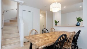 A dining area with a wooden table and chairs, a staircase, and a hanging light fixture.