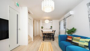 A modern living room with a blue sofa, a wooden coffee table, a TV, and a dining area with chairs and a table.