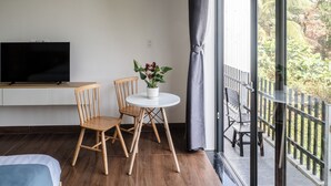 A modern room with a wooden floor, a bed, a TV, a small round table with chairs, and a potted plant. - T&H Hoi An Beach Villa (Da Nang)