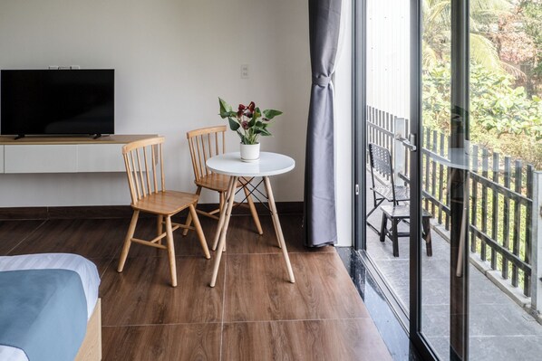 Une chambre moderne avec un plancher en bois, un lit, une télévision, une petite table ronde avec des chaises et une plante en pot.