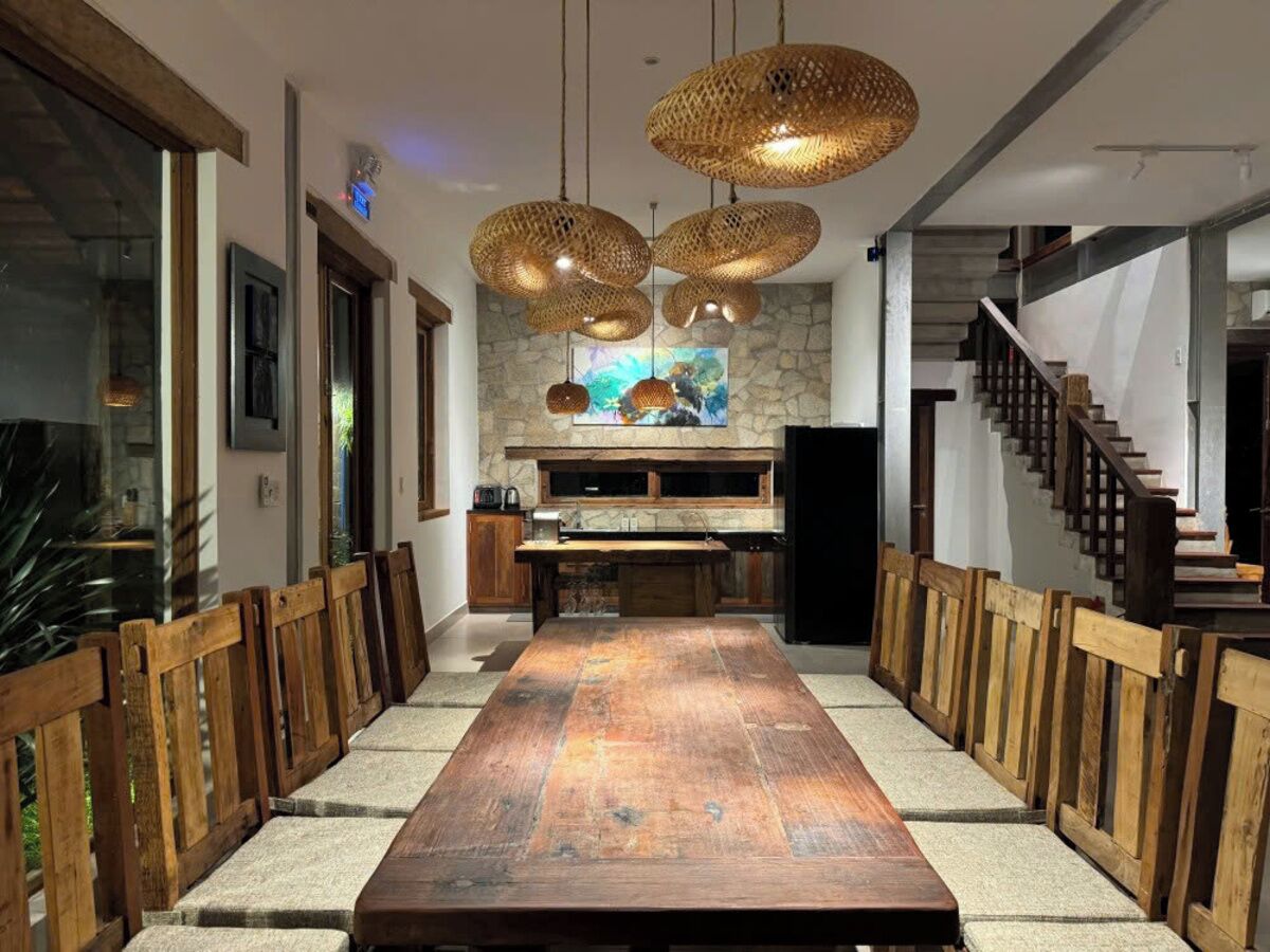 A long dining table with wooden chairs, a stone wall with a painting, and a staircase.