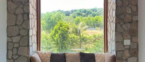 A stone-walled room with a large window overlooking a green landscape.