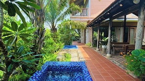 Ein Pool mit blauen Mosaikfliesen, umgeben von üppiger Vegetation und einem Gebäude mit einem gefliesten Dach.