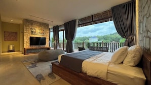 Ein Schlafzimmer mit Kamin aus Stein, einem Flachbildfernseher, einem großen Bett mit weißer Bettwäsche und einem Balkon mit Blick auf Grünflächen.