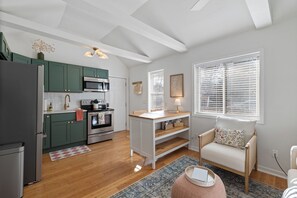 A modern kitchen with green cabinets, a wooden dining table, and a cozy seating area with a chair and ottoman.