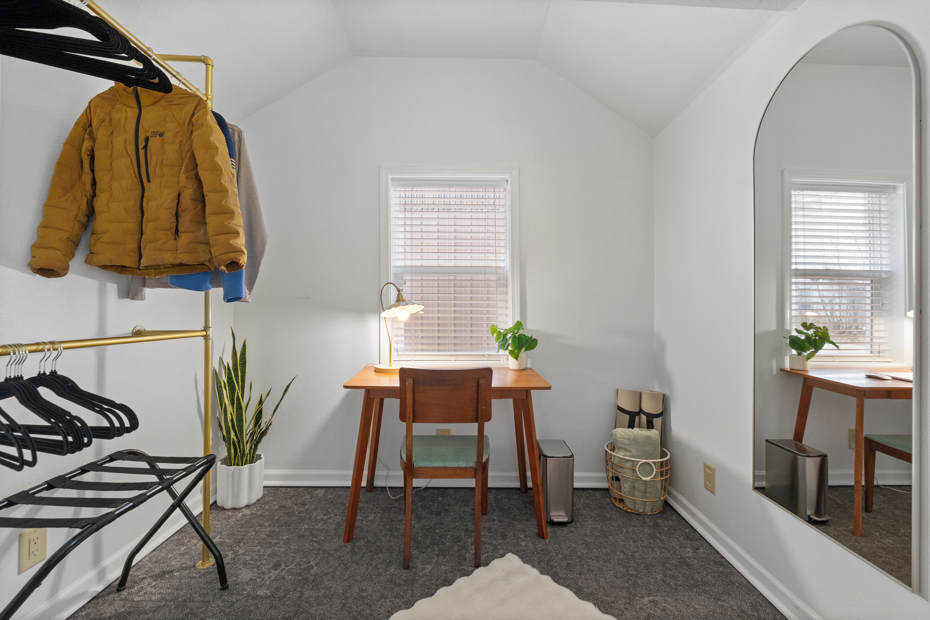 A room with a desk, chair, mirror, potted plants, and a coat rack.
