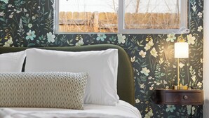 A bedroom with a bed, pillows, a bedside table with a lamp, and floral wallpaper.
