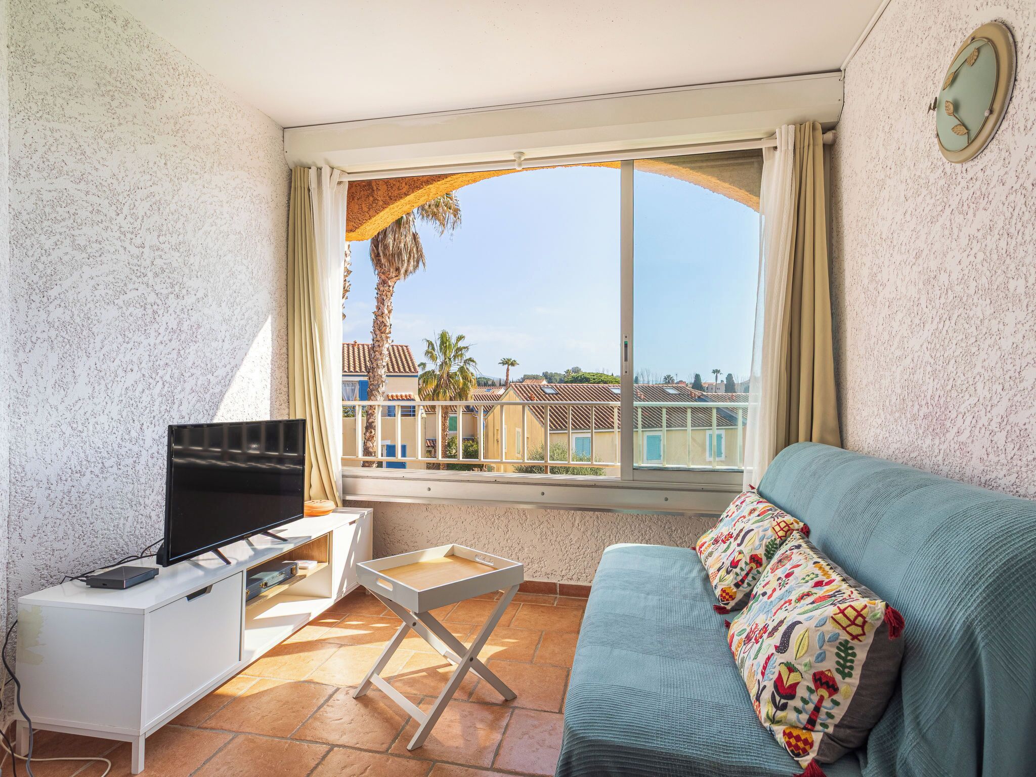 A balcony with a TV, a small table, and a sofa with colorful cushions.