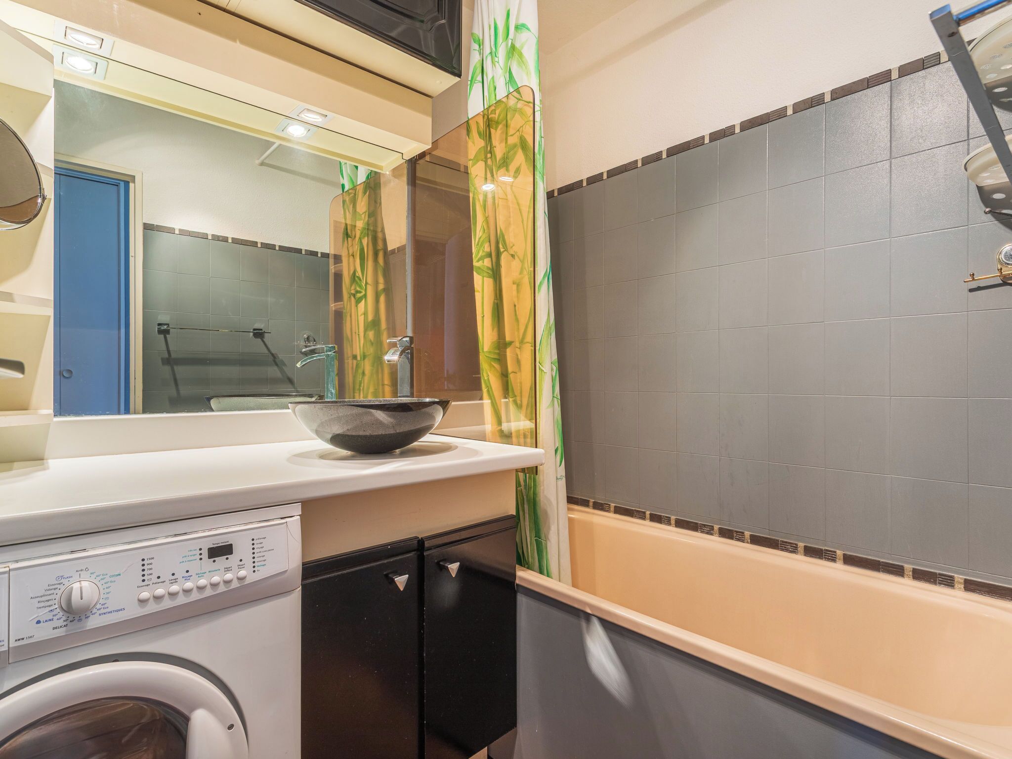 Une salle de bain moderne avec un grand miroir, un lavabo agrémenté d’un récipient décoratif, un lave-linge et une baignoire.