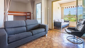 Una habitación moderna con un sofá gris, una silla negra, un ventilador de techo, una litera y un balcón con vistas.