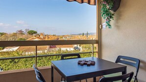 Un balcón con una mesa y sillas, vista panorámica de la ciudad y una planta colgante.