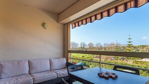 Un balcón con sofá y mesa, vista a un jardín y cielo despejado.