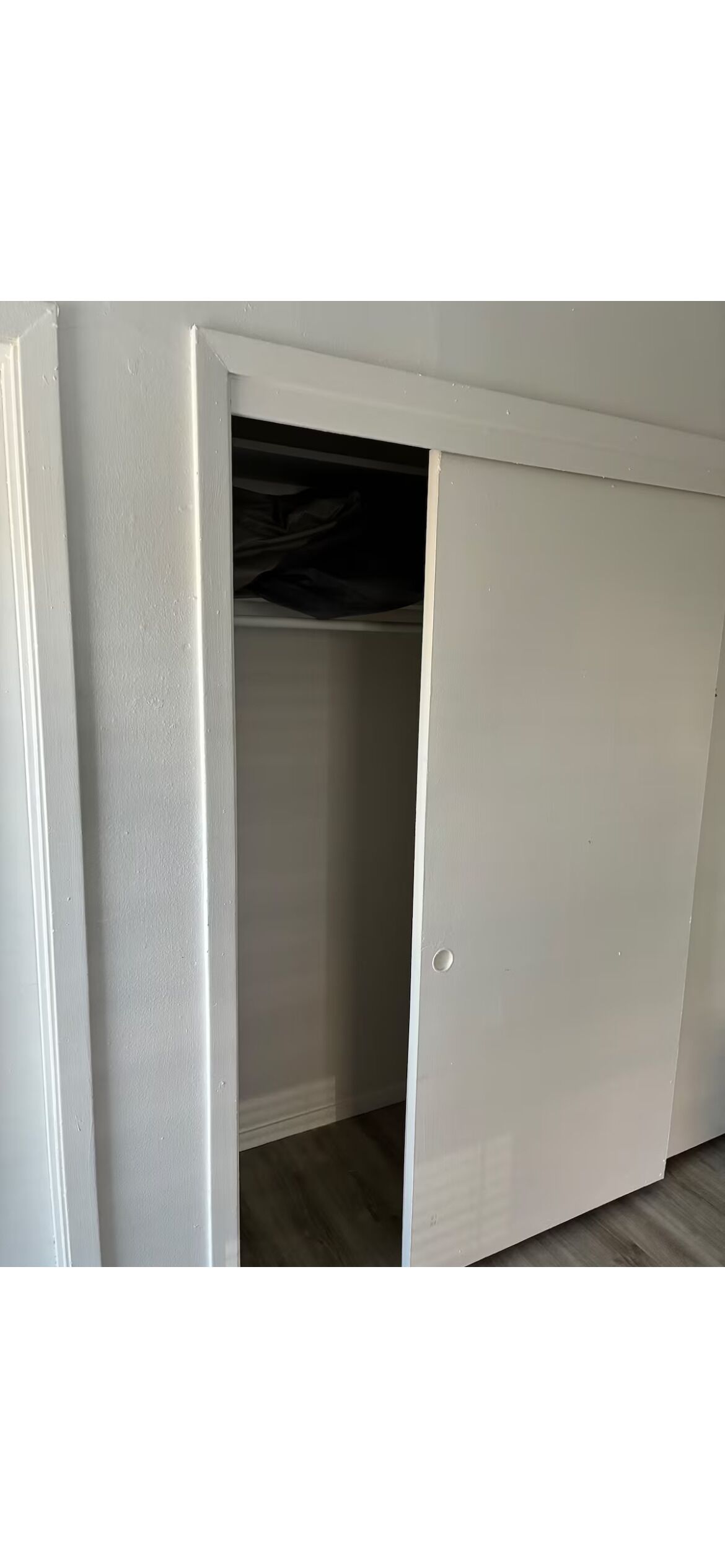Un armario blanco con puerta corredera, una repisa visible y una prenda colgada de color oscuro.