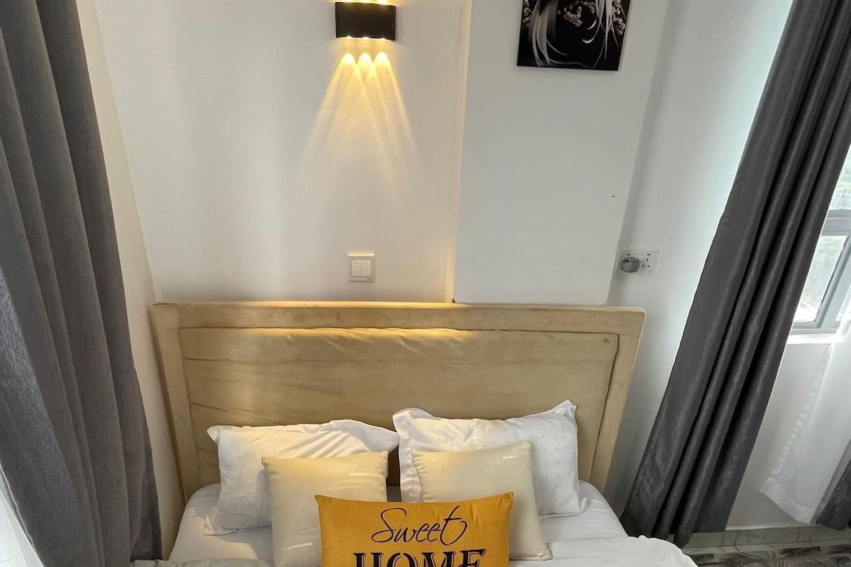 Un lit bien fait, avec une tête de lit, un luminaire fixé au mur et une œuvre d’art encadrée au-dessus.