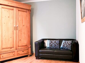 Ein Zimmer mit einem Holzschrank und einem schwarzen Ledersofa mit gemusterten Kissen.
