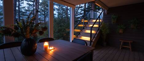 A wooden deck with a table and chairs, a candle, and a staircase leading to an upper level.