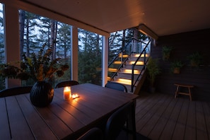 Una terraza de madera con una mesa, sillas, una vela y una escalera que sube a un nivel superior.