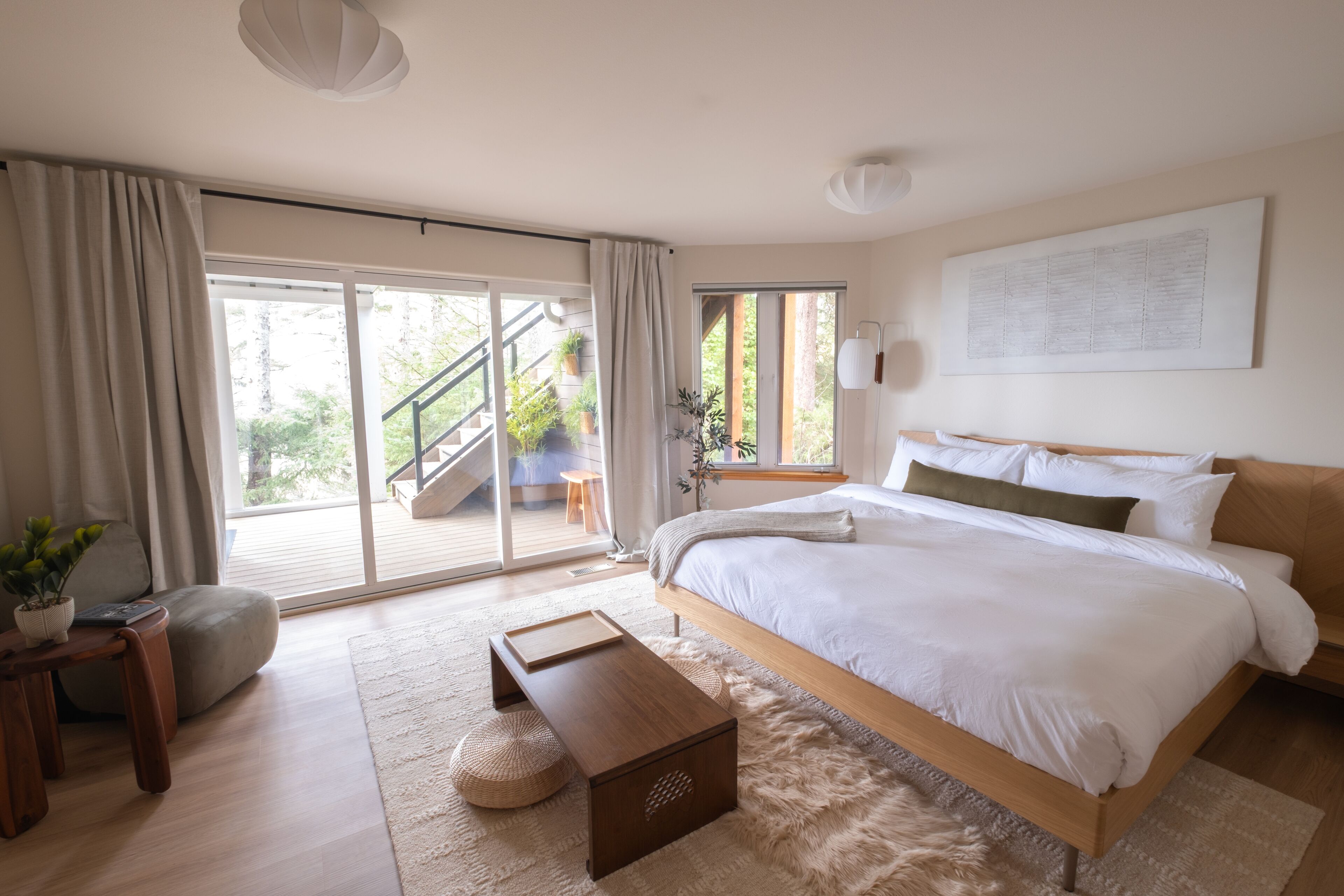 A modern bedroom with a large bed, a sliding glass door to a balcony, and a view of the outdoors.