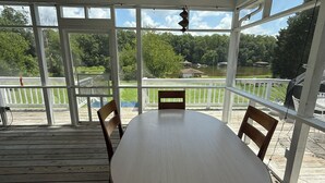 Un espace extérieur abrité, doté d’une table ronde et de chaises, offrant une vue sur un lac et la verdure environnante.
