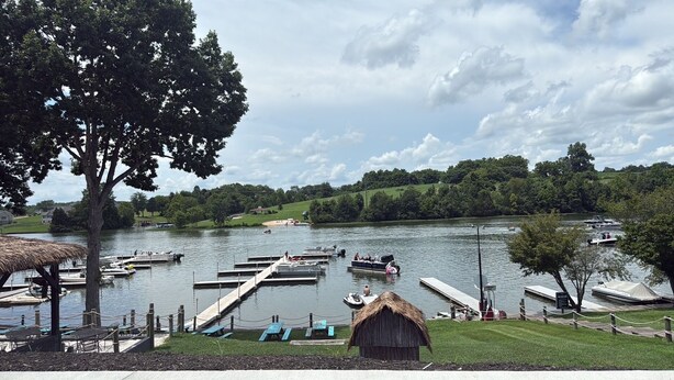 Un parc au bord du lac, avec des bateaux amarrés, des tables de pique-nique et un abri à toit de chaume.
