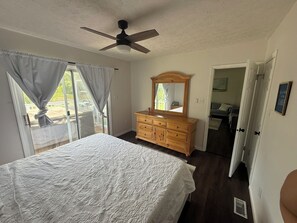 Ein Schlafzimmer mit Bett, Schminktisch, Deckenventilator und Blick durch ein Fenster.