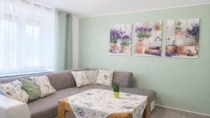 Uma sala de estar com um sofá modular, uma mesa pequena com toalha de mesa florida e três obras de arte florais penduradas na parede.
