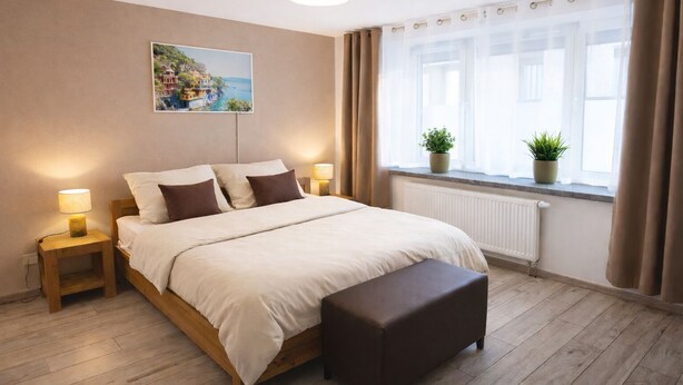 Quarto com cama, abajures, janela com cortinas, radiador e planta em vaso.