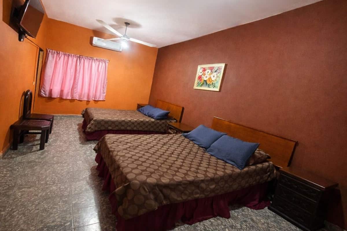 A hotel room with two beds, a ceiling fan, a TV mounted on the wall, a chair, and a window with curtains.