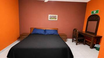 Quarto com cama, escrivaninha, cadeira, ventoinha no teto e um quadro na parede.