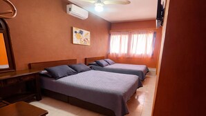 Habitación de hotel con dos camas, ventilador de techo, equipo de aire acondicionado, televisor y un cuadro en la pared.